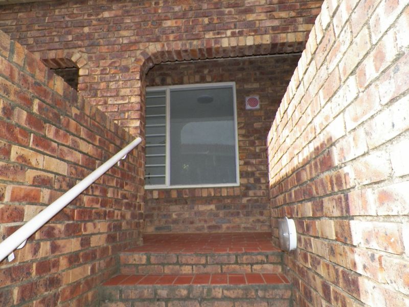 A brick-constructed entrance area featuring a staircase with a metal handrail and a security-screened window.
