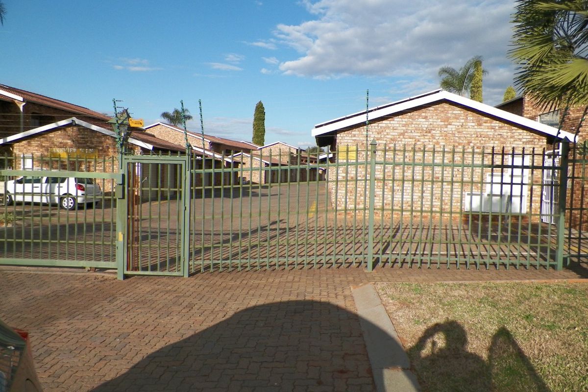 Front entrance view of the apartment complex featuring a secure metal gate, electric fencing, and paved driveway access.