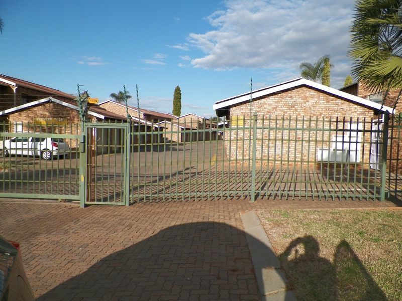 Front entrance view of the apartment complex featuring a secure metal gate, electric fencing, and paved driveway access.