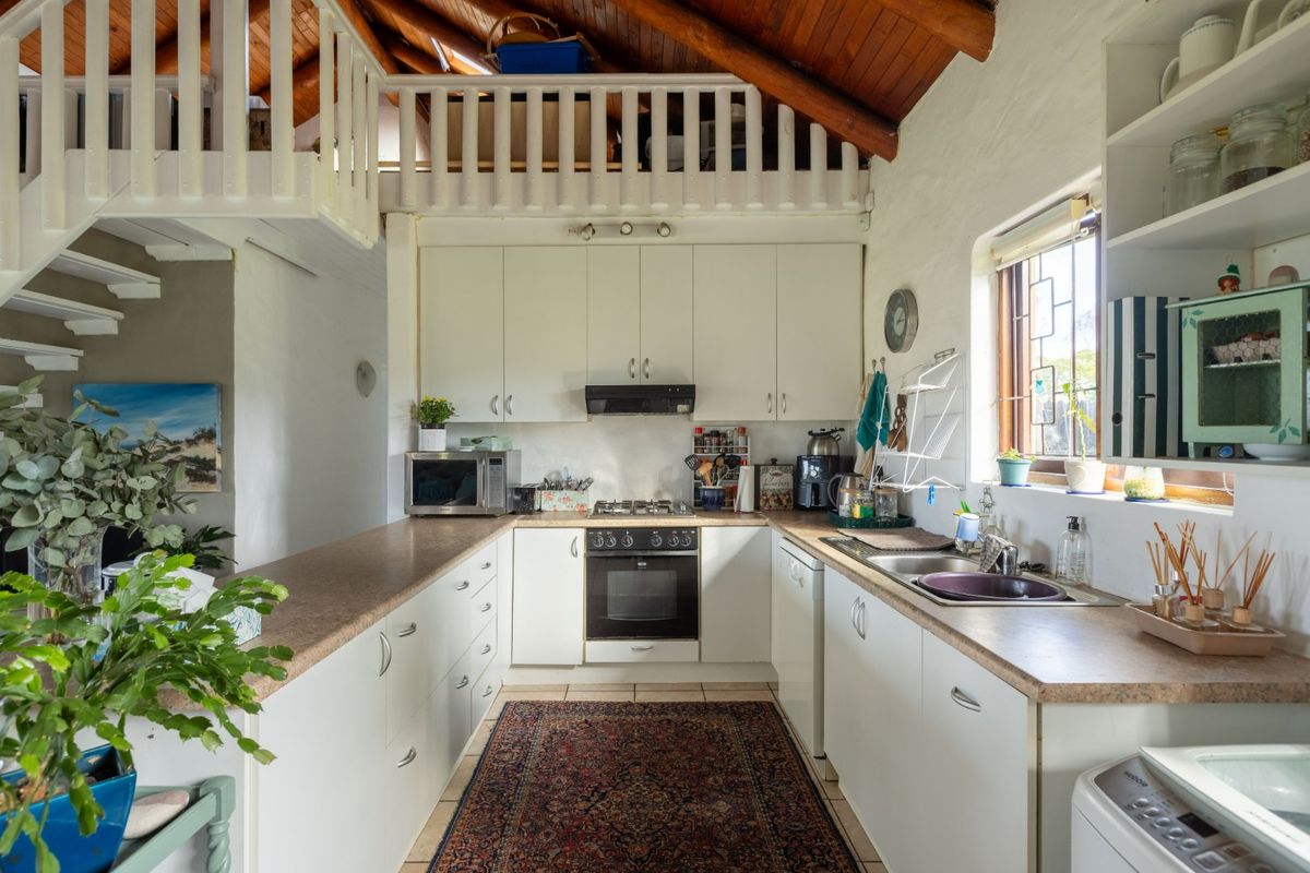 A functional kitchen featuring white cabinetry, built-in oven and hob, and a unique mezzanine level with exposed timber ceiling beams.
