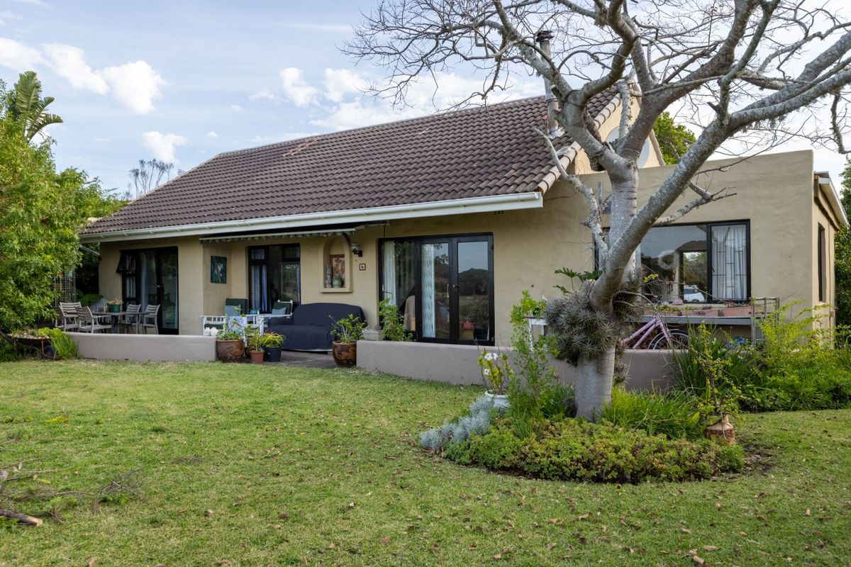 Rear view of a single-story house featuring a tiled roof, plastered exterior walls, and a paved patio area overlooking a garden.