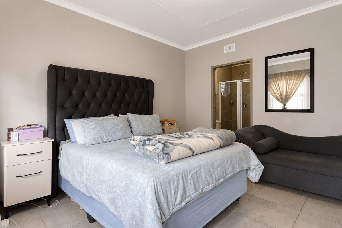 A well-maintained bedroom featuring neutral wall tones, tiled flooring, and direct access to an en-suite bathroom.