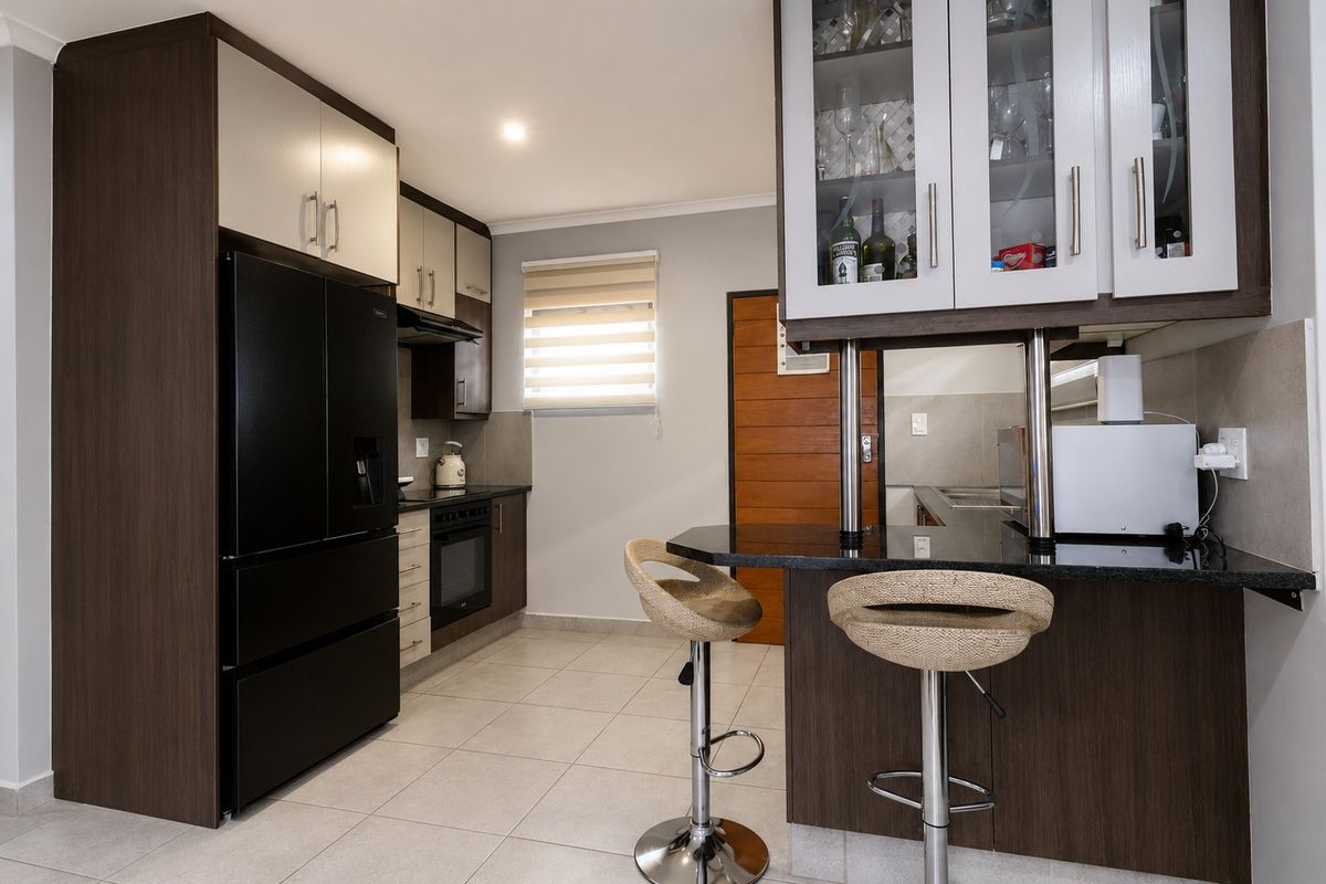 Modern kitchen featuring dark wood and light cabinetry, granite countertops, a breakfast bar, and integrated appliances with neutral tiled flooring.