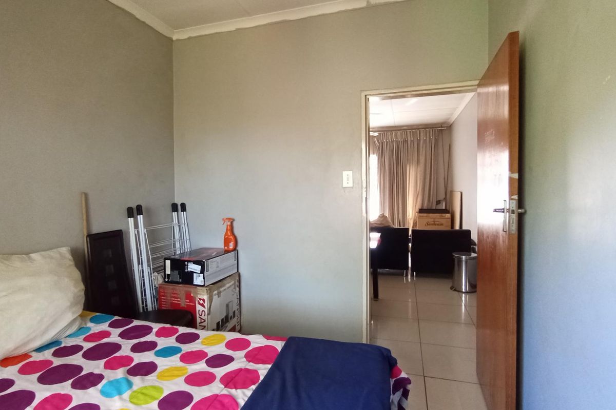 A bedroom featuring tiled flooring and a doorway leading to an adjacent living area, showing signs of wear on the walls and ceiling.