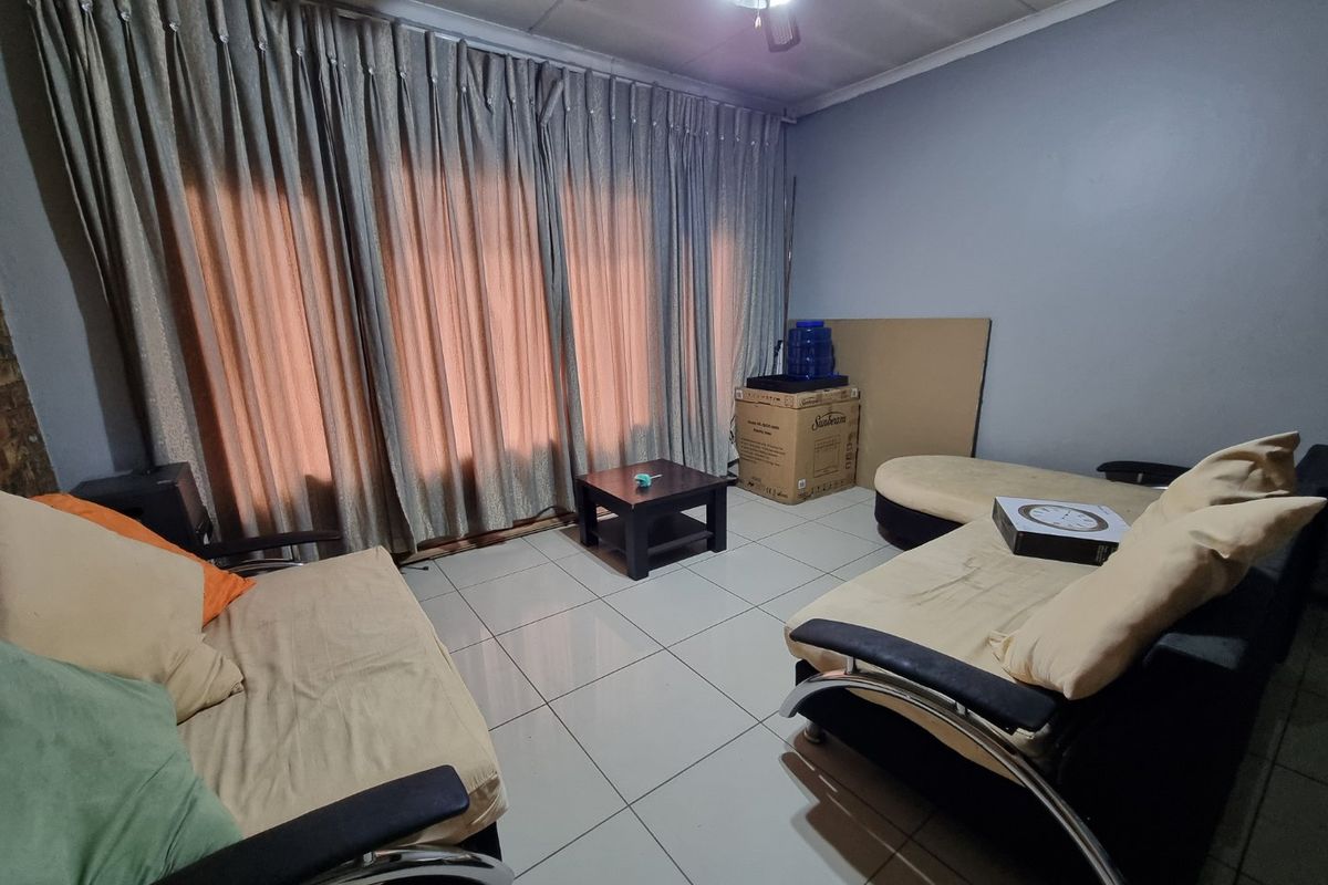 A living room featuring tiled flooring and a ceiling fan, with large window curtains providing natural light control.