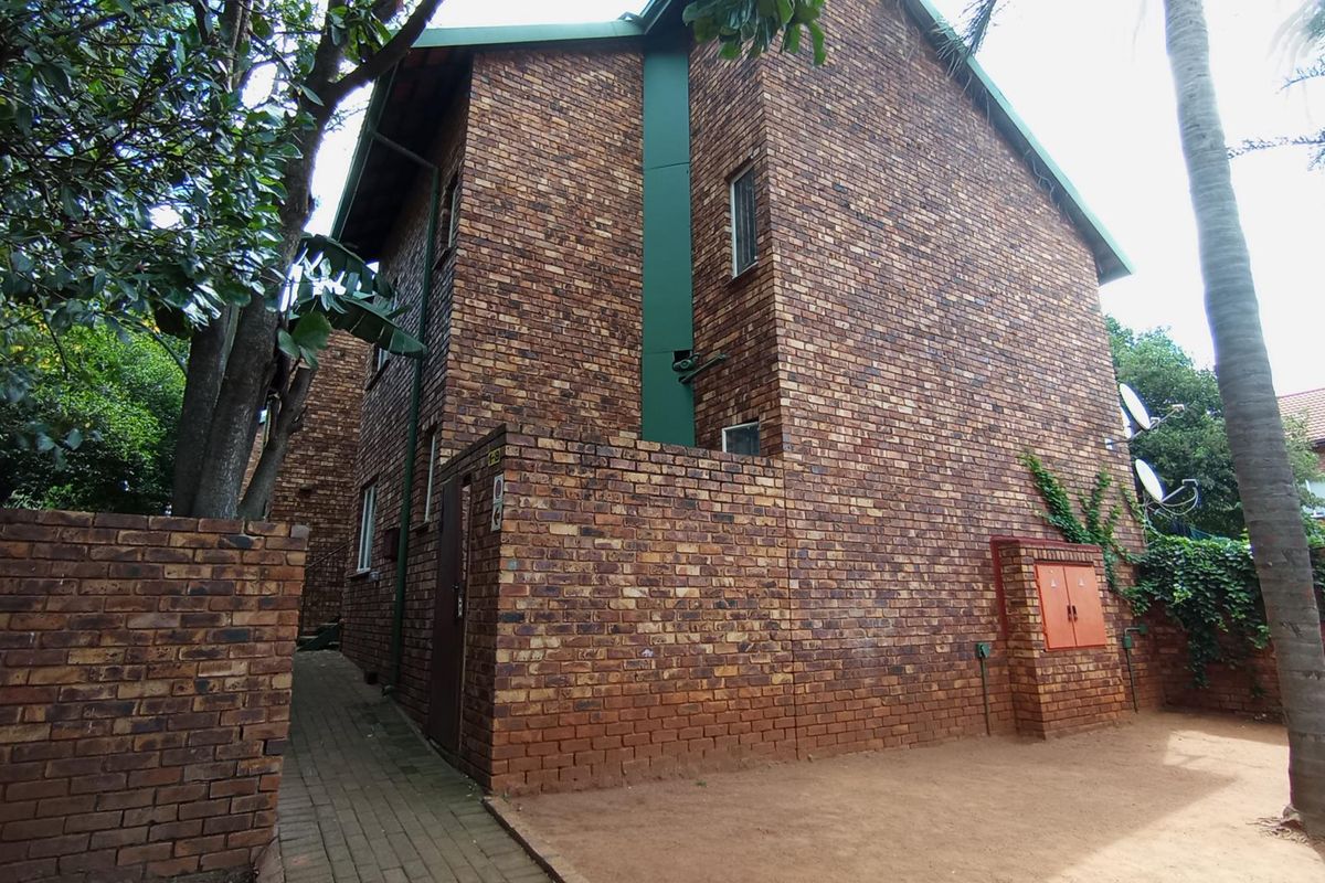 Exterior view of the apartment building featuring a face brick facade, pitched roof, and a paved walkway leading along the side of the structure.
