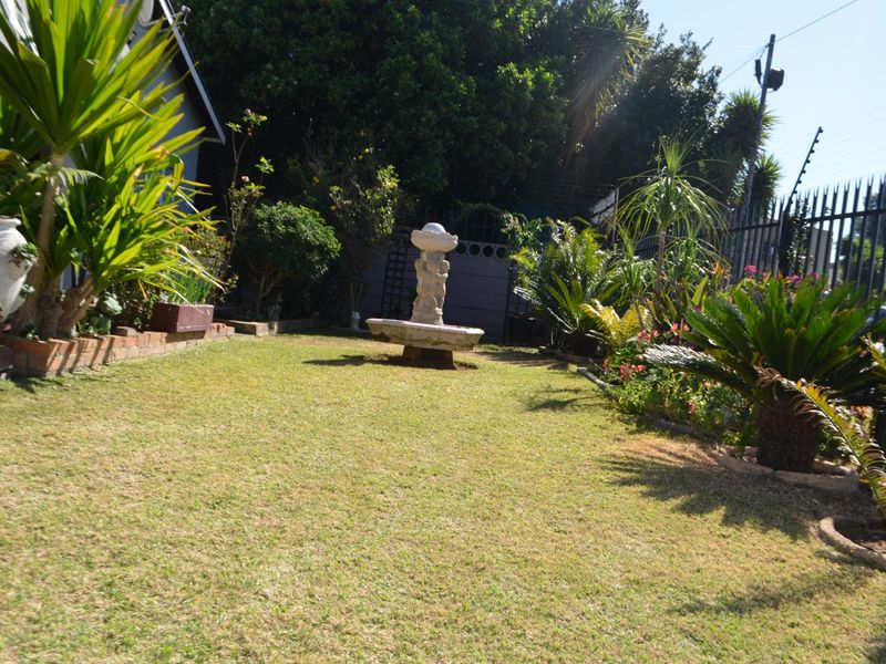 A well-maintained garden area featuring a central stone fountain, established landscaping, and secure perimeter fencing.