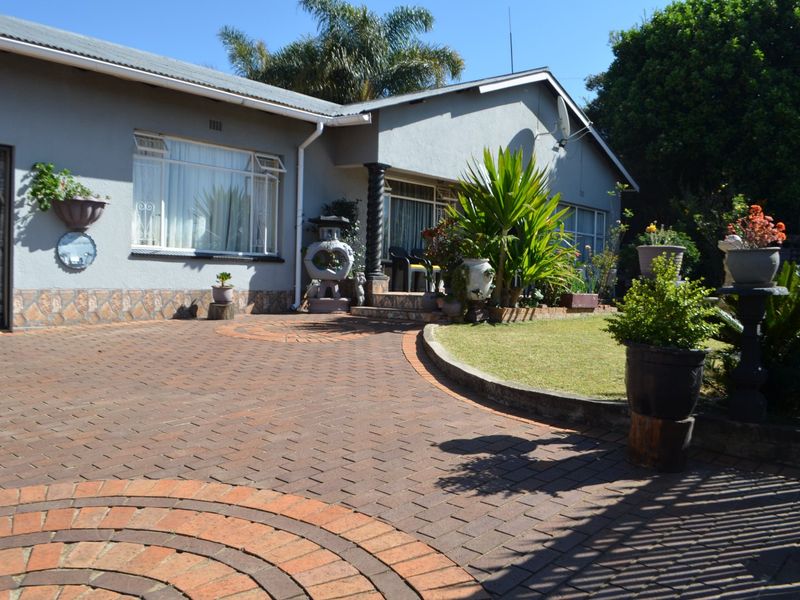 Front view of the house featuring a paved driveway, well-maintained garden, and brick facade with a metal roof.