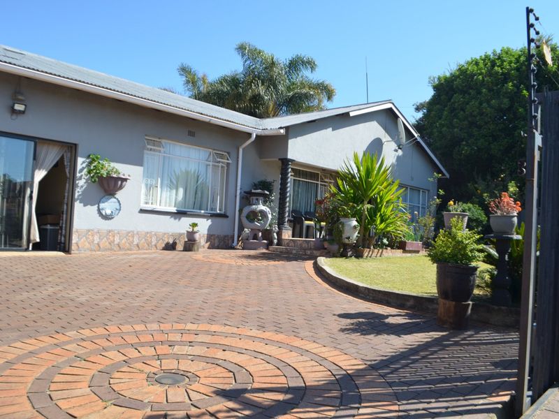 Front view of the property featuring a paved circular driveway, landscaped lawn, and secure perimeter fencing with an integrated security gate.