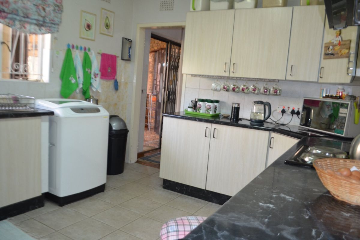 A functional kitchen featuring laminate cabinetry, granite countertops, and tiled flooring, with a dedicated space for laundry appliances.