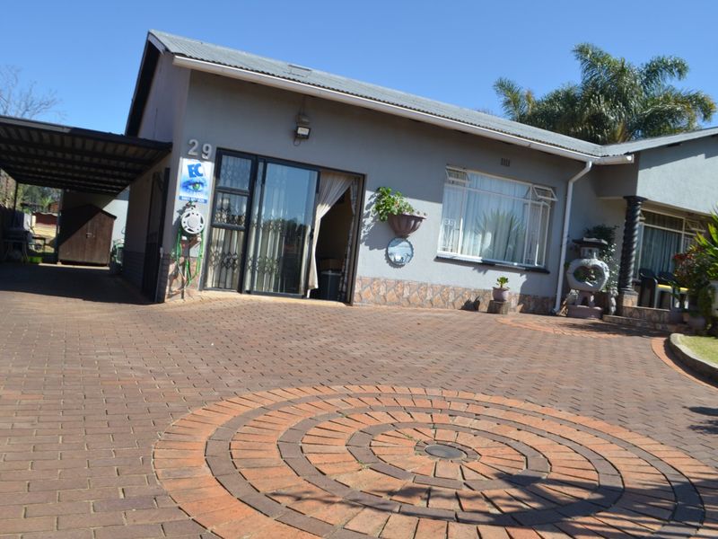 Front exterior view of the house featuring a paved driveway, attached carport, and secure sliding door entrance.