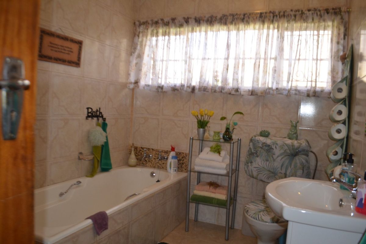 A functional bathroom featuring a built-in bathtub, pedestal washbasin, toilet, and full-height ceramic wall tiling.