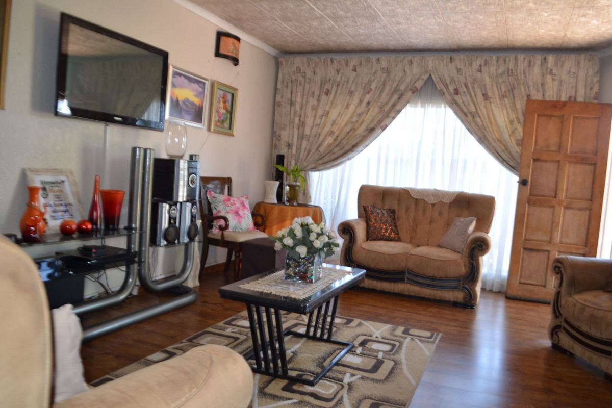 A living room featuring laminate flooring and a textured ceiling, with a wooden door leading to the exterior.