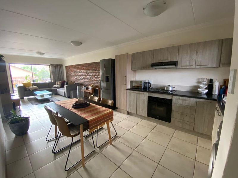 Open-plan living and kitchen area featuring modern cabinetry, built-in appliances, tiled flooring, and an exposed brick feature wall leading to a balcony.