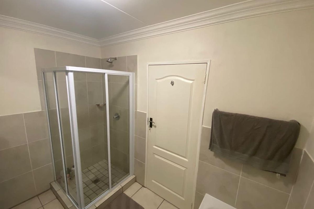 A functional bathroom featuring a glass-enclosed shower, neutral wall and floor tiling, and classic cornice detailing.