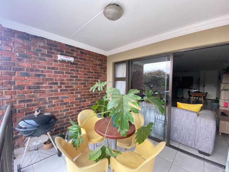 A covered balcony featuring an exposed brick wall, tiled flooring, and sliding glass door access to the interior living space.