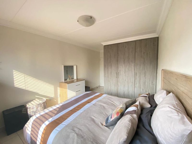 A well-lit bedroom featuring neutral walls, tiled flooring, and ample built-in cupboard storage space.