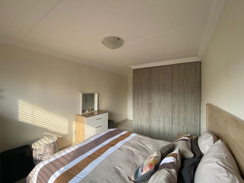 A well-maintained bedroom featuring neutral walls, coving, and ample built-in cupboard storage with a wood-grain finish.