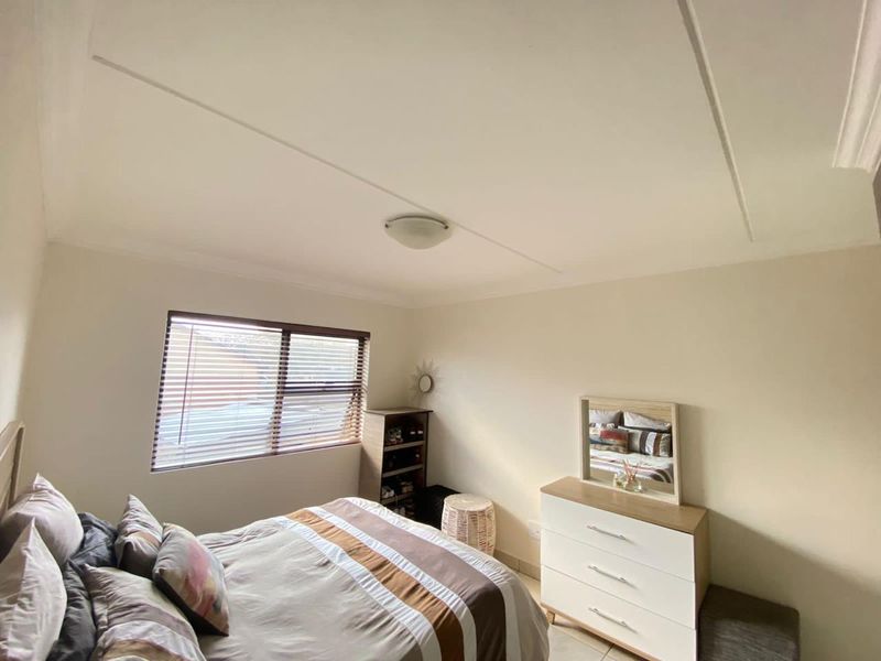 A well-lit bedroom featuring neutral walls, tiled flooring, and a window fitted with venetian blinds.
