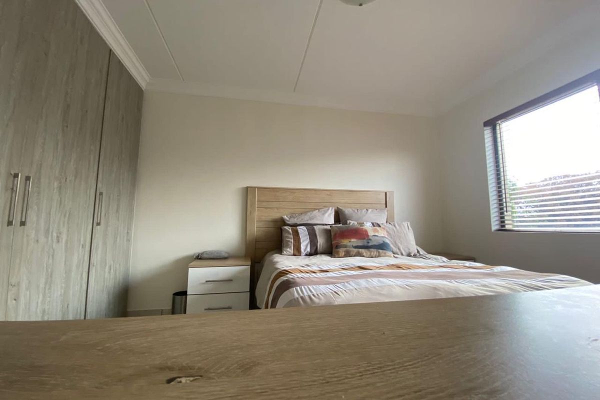 A well-lit bedroom featuring built-in cupboards, neutral wall finishes, and venetian blinds, providing a clean and functional living space.