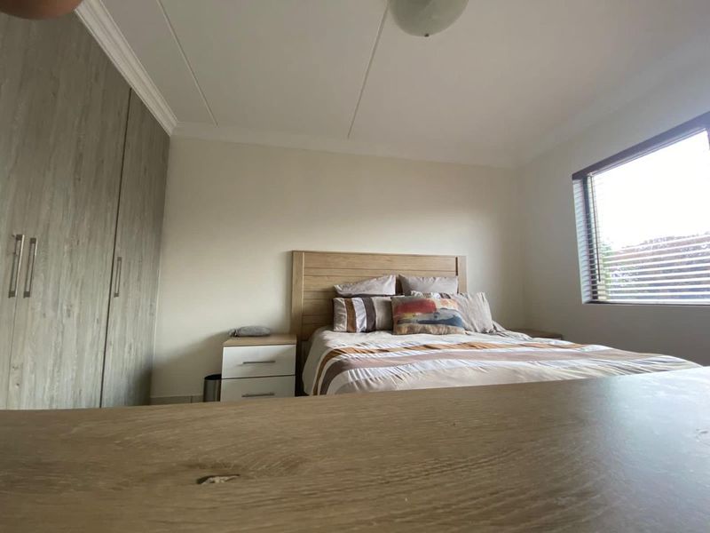 A well-lit bedroom featuring built-in cupboards, neutral wall finishes, and venetian blinds, providing a clean and functional living space.