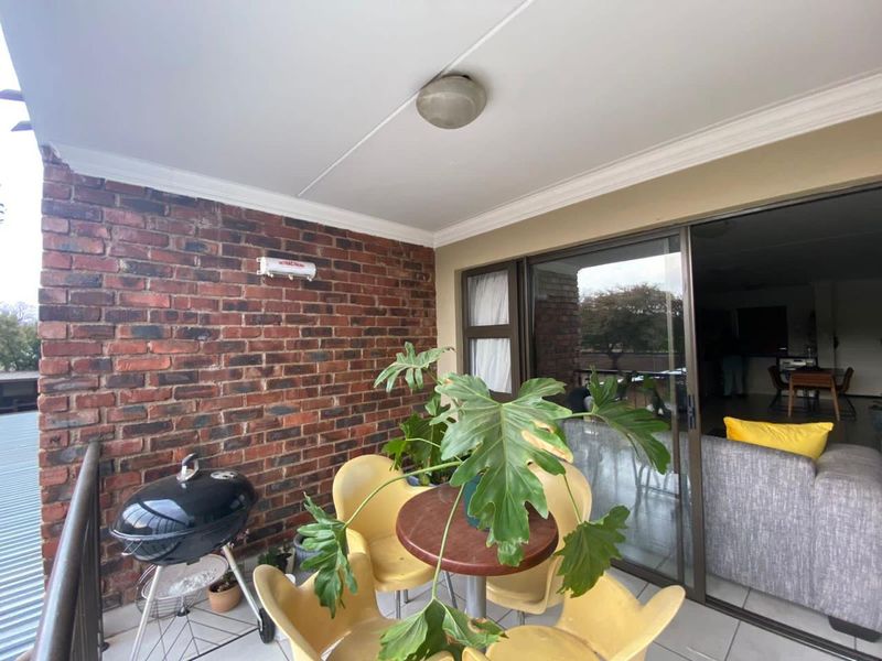 A covered balcony featuring an exposed brick wall, tiled flooring, and sliding glass door access to the interior living area.