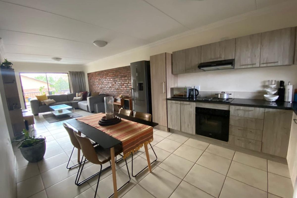 Open-plan living and kitchen area featuring tiled floors, modern cabinetry, a built-in oven and hob, and an exposed brick feature wall.