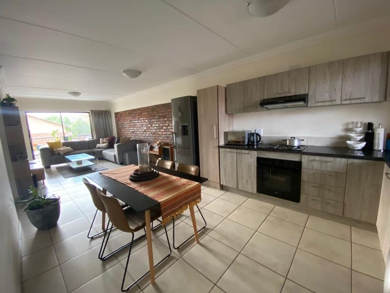 Open-plan living and kitchen area featuring tiled floors, modern cabinetry, a built-in oven and hob, and an exposed brick feature wall.