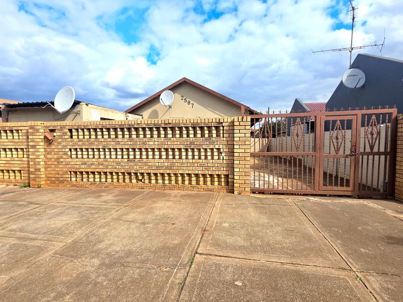 Front view of the property featuring a paved driveway, a decorative face-brick boundary wall, and a secure metal entrance gate.