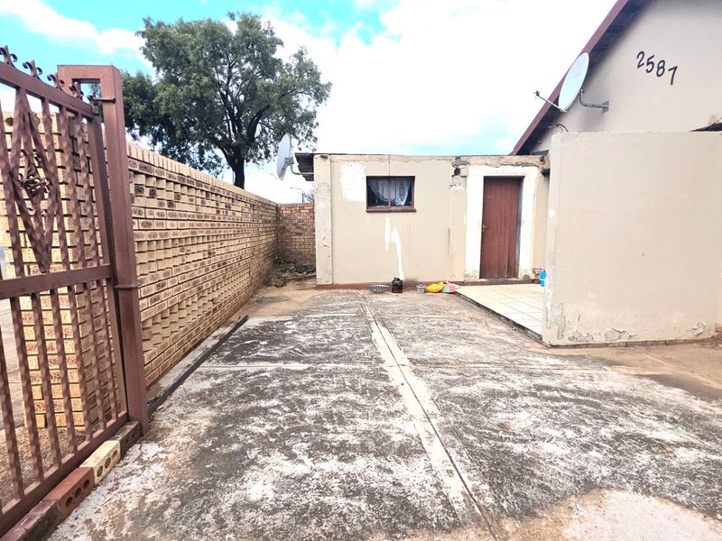 Exterior view of the property featuring a concrete driveway, brick boundary wall, and metal security gate.