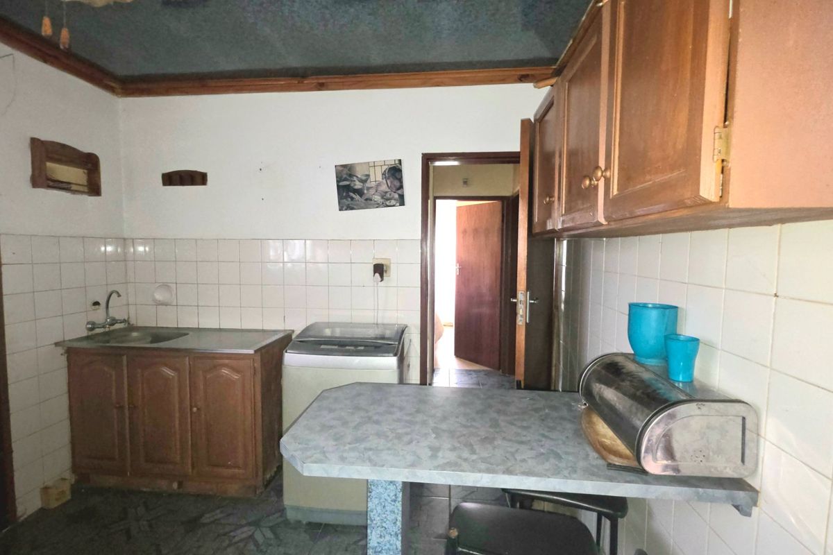 A dated kitchen featuring wooden cabinetry, tiled splashbacks, and a breakfast bar, offering potential for modernization and renovation.