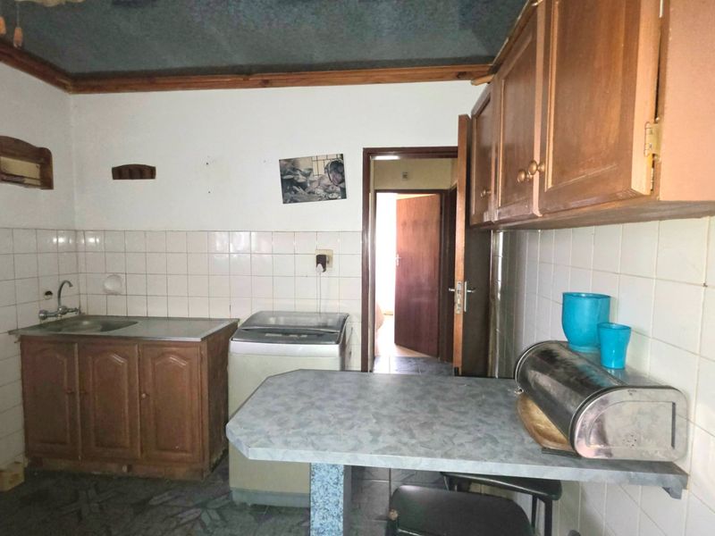 A dated kitchen featuring wooden cabinetry, tiled splashbacks, and a breakfast bar, offering potential for modernization and renovation.