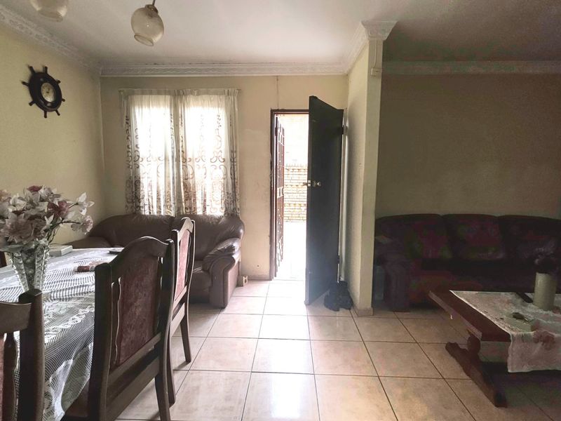 An open-plan living and dining area featuring tiled flooring, crown molding, and direct access to an exterior space.