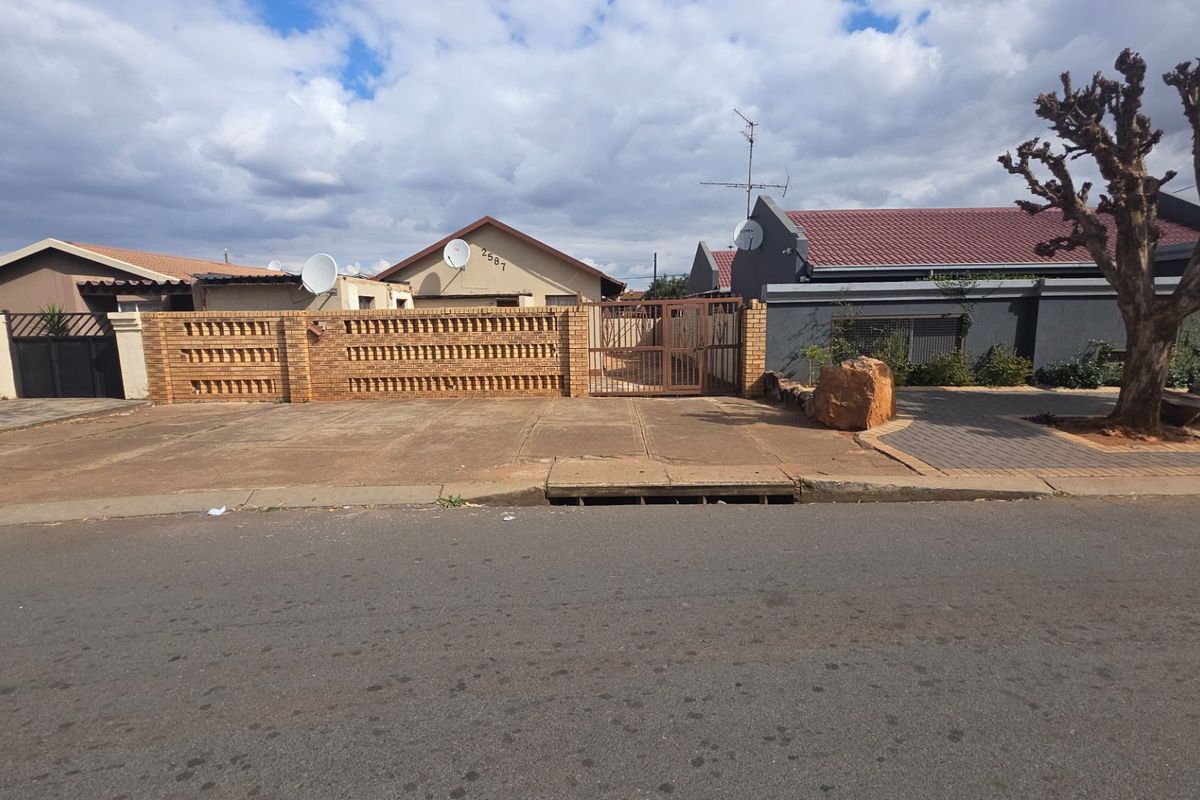 Street view of the property featuring a brick boundary wall, metal entrance gate, and paved driveway area.