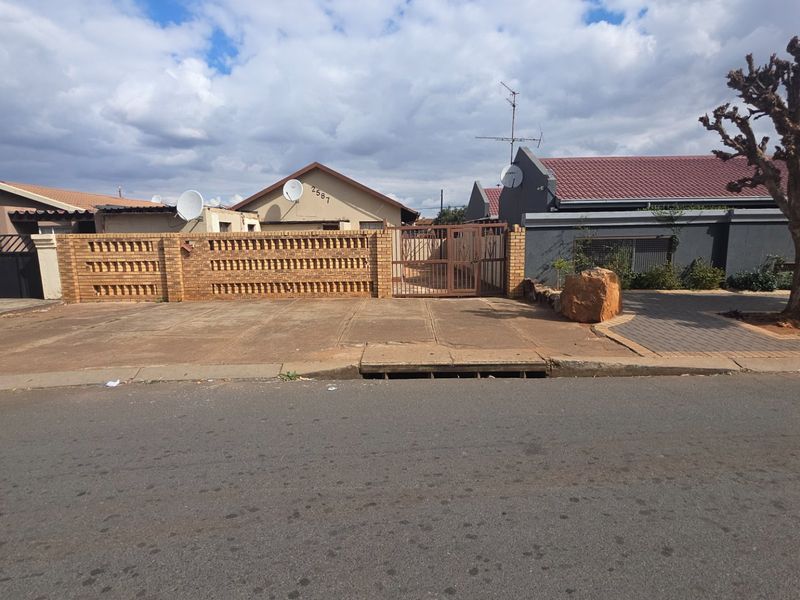 Street view of the property featuring a brick boundary wall, metal entrance gate, and paved driveway area.