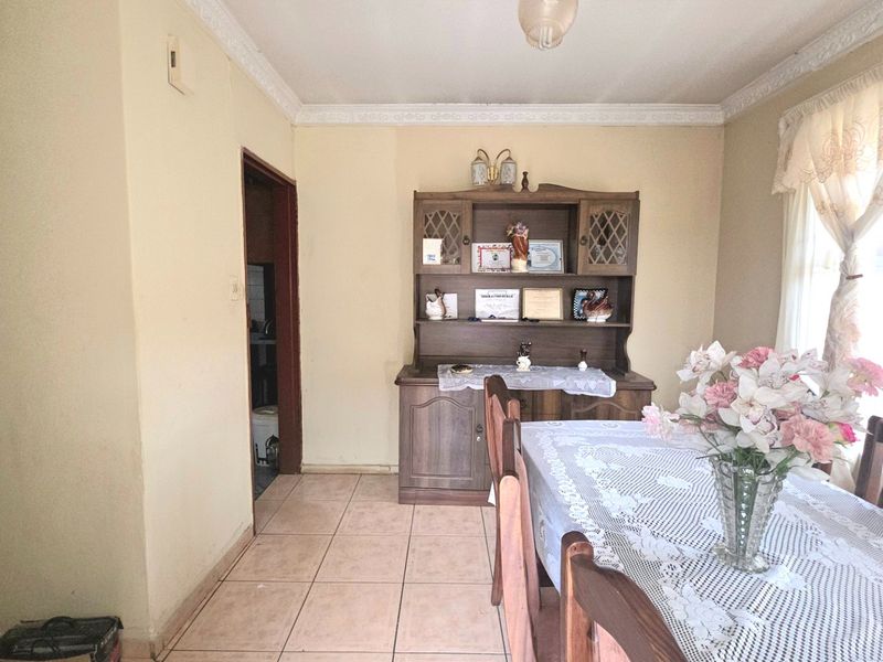 A dining room featuring tiled flooring, decorative ceiling cornicing, and a doorway leading to an adjacent utility space.