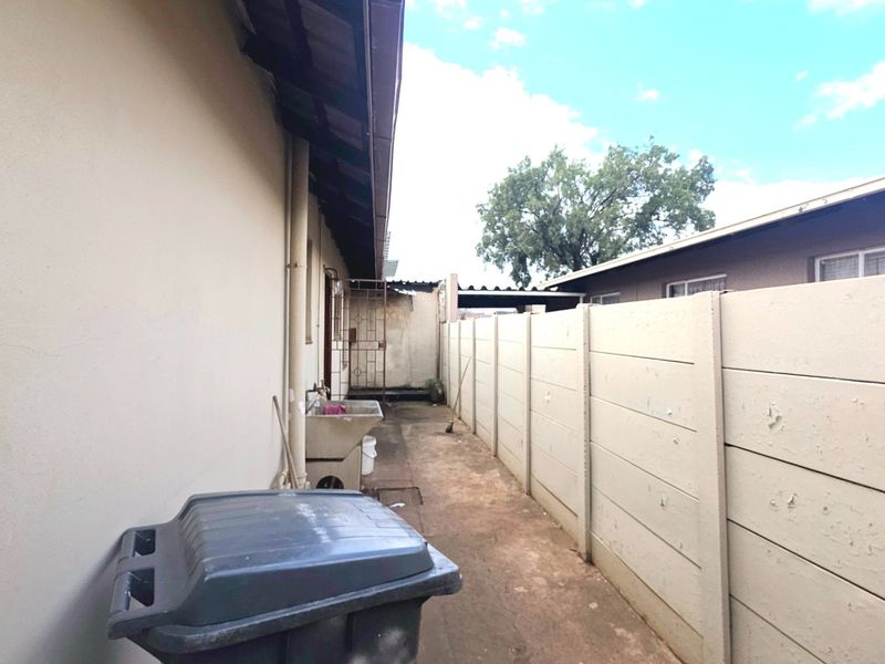 A narrow side exterior passage featuring a concrete utility sink, paved flooring, and a high precast concrete boundary wall.