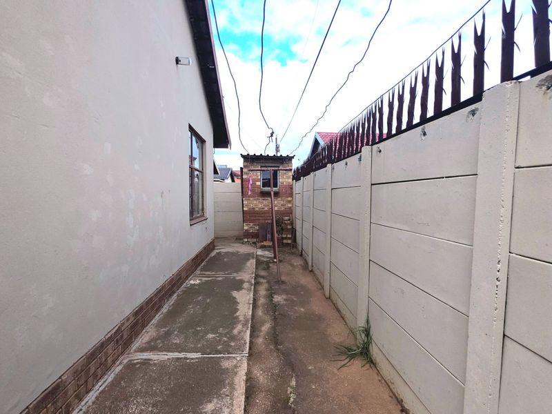 A narrow side passage of the property featuring a concrete walkway, perimeter precast walling with security spikes, and an exterior utility structure.