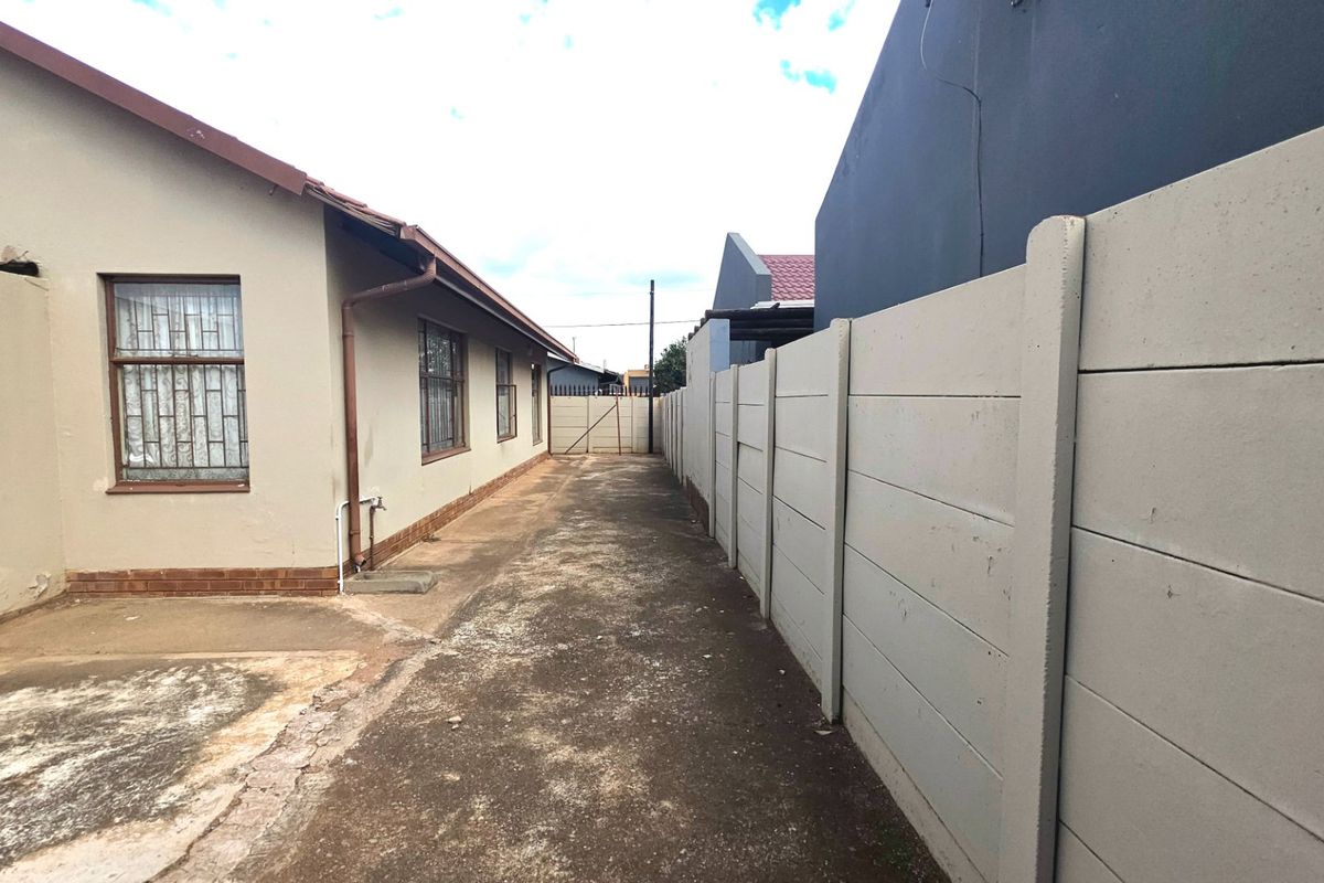 Side exterior walkway featuring concrete paving and a high precast concrete boundary wall along the property perimeter.