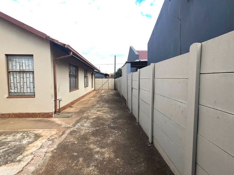 Side exterior walkway featuring concrete paving and a high precast concrete boundary wall along the property perimeter.