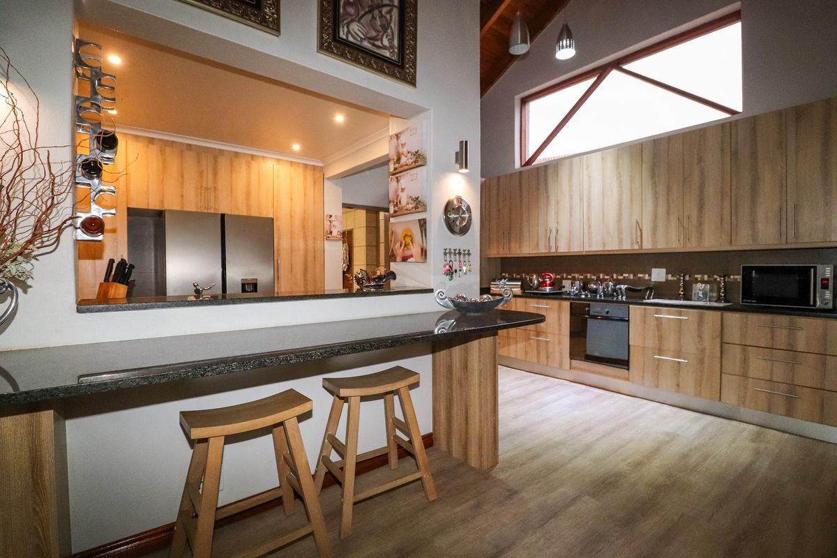 Modern kitchen featuring light wood cabinetry, dark stone countertops, a breakfast bar, and high vaulted ceilings with integrated lighting.