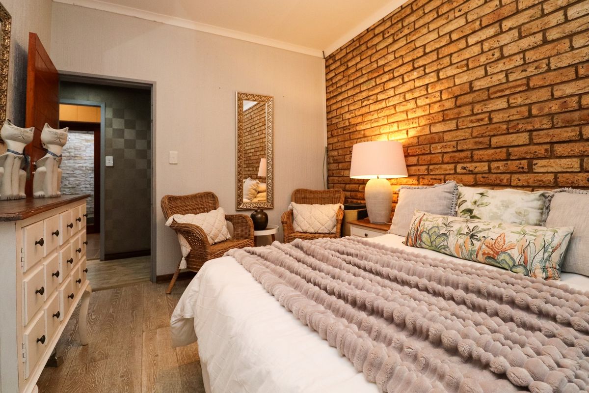 A cozy bedroom featuring a rustic exposed brick feature wall, wood-look flooring, and a doorway leading to an adjacent space.