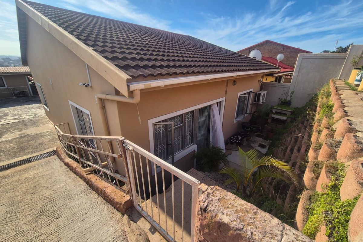Rear view of the property featuring a tiled roof, security gates, and a tiered retaining wall structure.