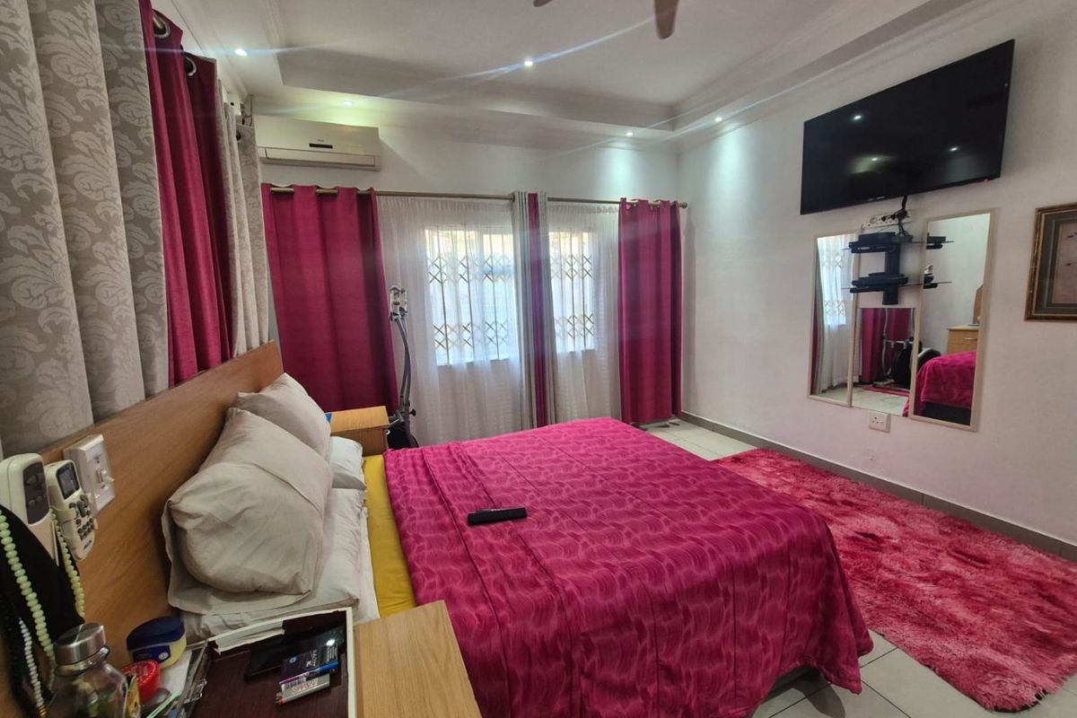 A well-maintained bedroom featuring tiled flooring, a ceiling fan, and a wall-mounted air conditioning unit, providing a comfortable and functional living space.