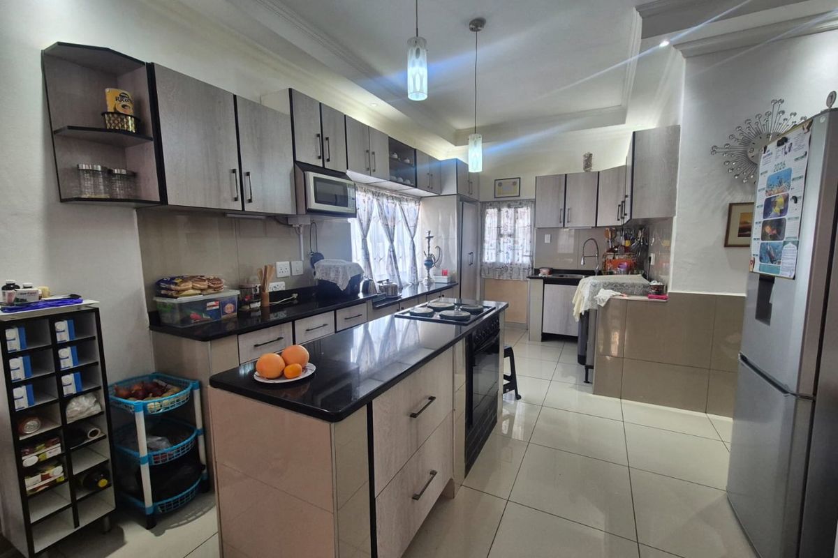 Modern kitchen featuring extensive built-in cabinetry, granite countertops, a central island with a hob, and tiled flooring throughout.