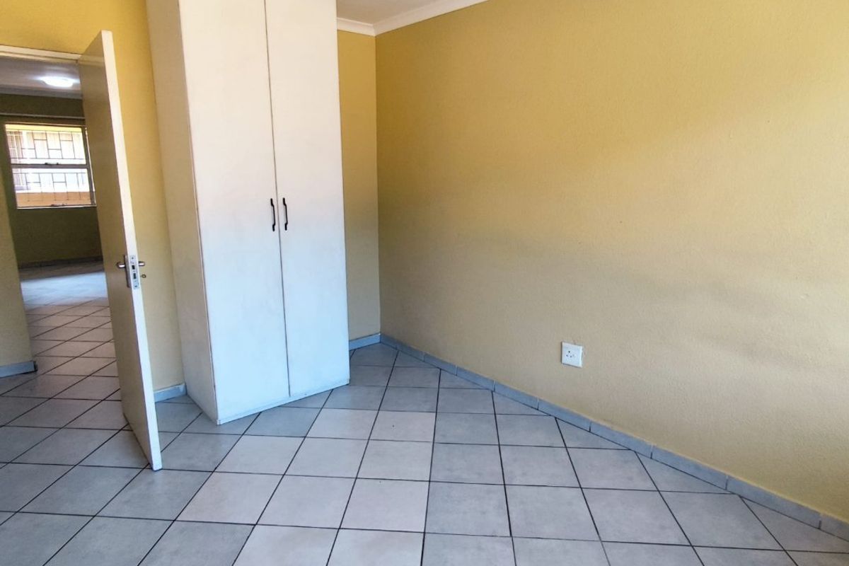 A simple bedroom featuring tiled flooring, a built-in wardrobe, and neutral wall tones, offering a clean and functional living space.