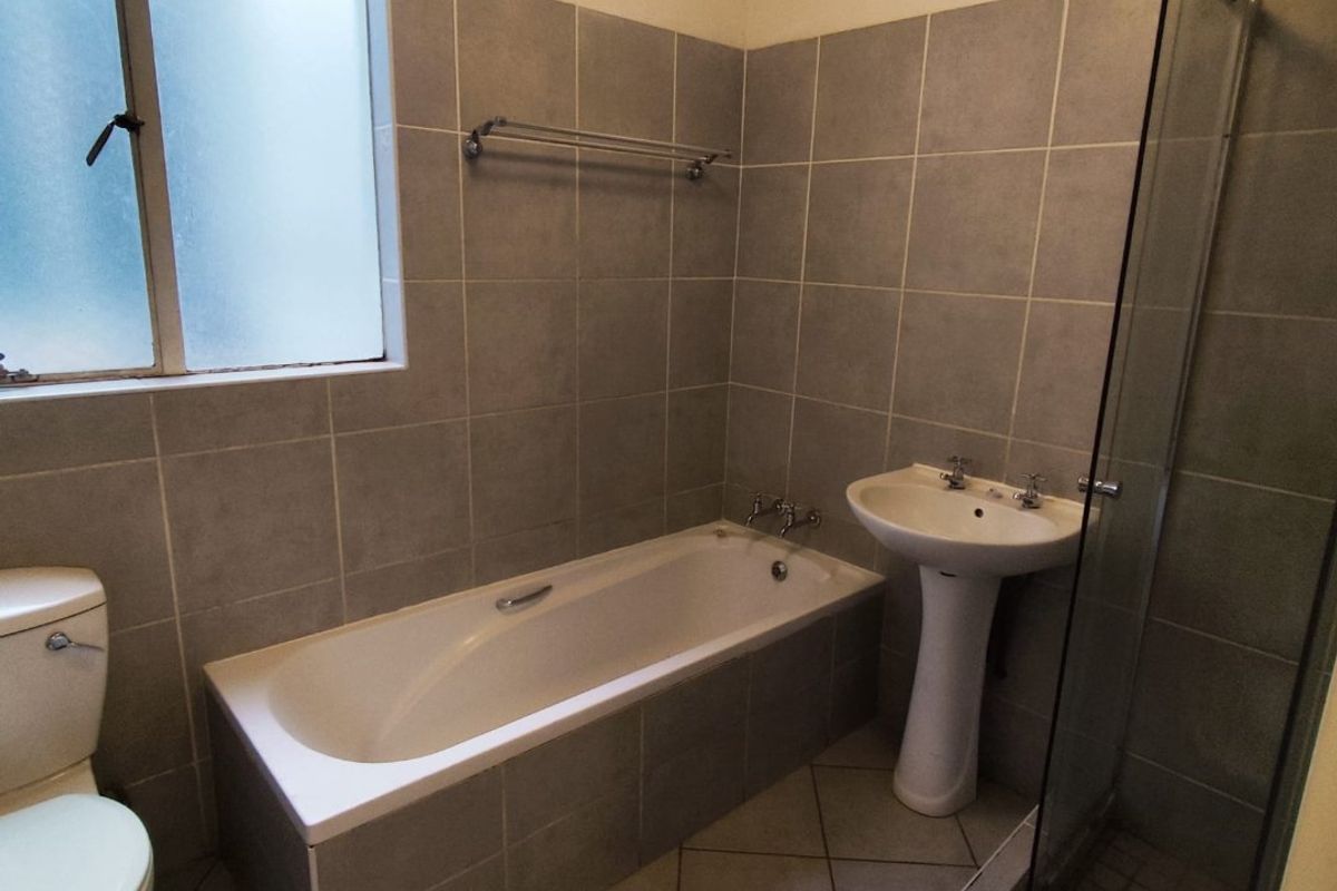 A functional bathroom featuring a tiled bathtub, pedestal basin, separate glass-enclosed shower, and neutral wall tiling.