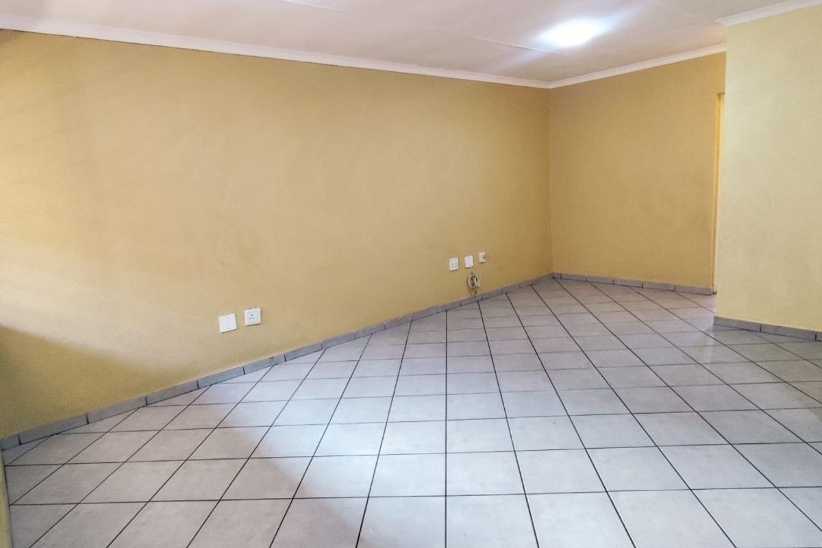 A spacious, empty living area featuring neutral-toned walls, tiled flooring, and recessed ceiling lighting, providing a versatile blank canvas for interior design.