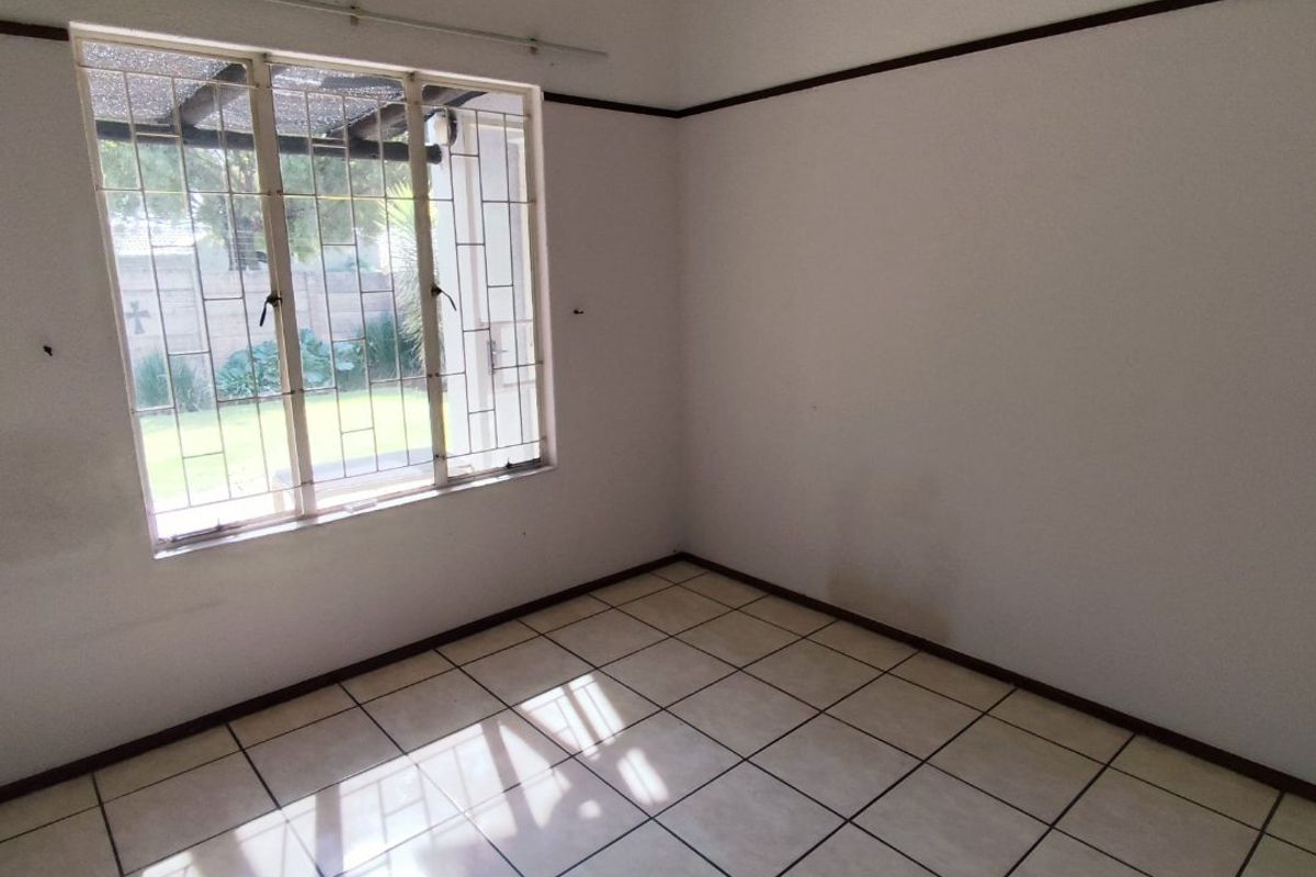 An empty bedroom featuring tiled flooring, a security-barred window, and a simple ceiling-mounted light fixture.