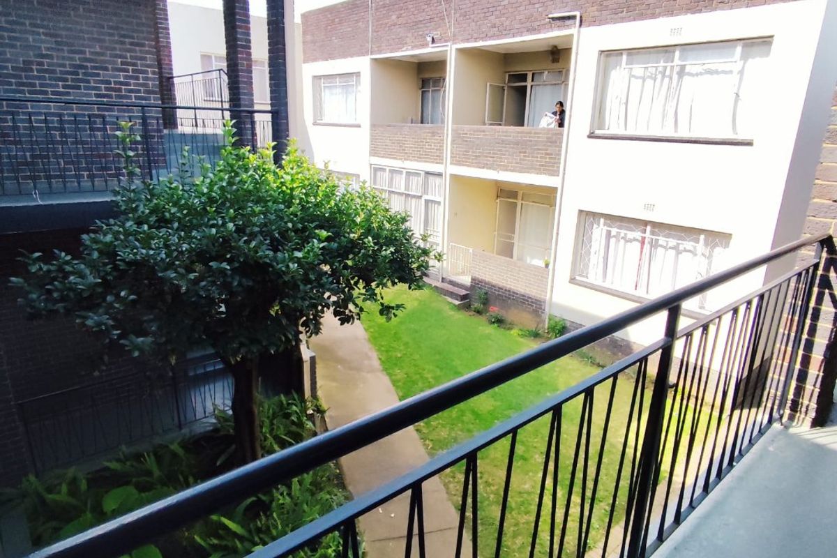 View of the apartment complex courtyard featuring a central garden, concrete pathway, and brick building facades with metal balcony railings.
